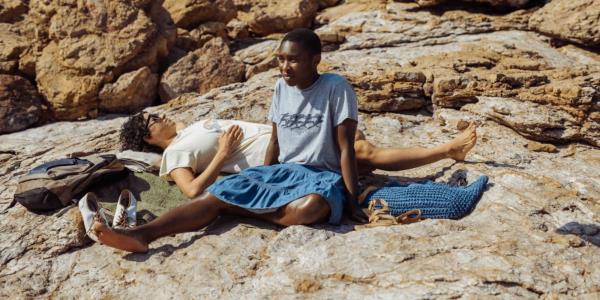 Cynthia Erivo and Alia Shawkat sit on rocks near the beach in Drift