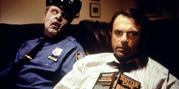 Sam Neill, with a book open on his chest, sits next to a zombie in In The Mouth of Madness