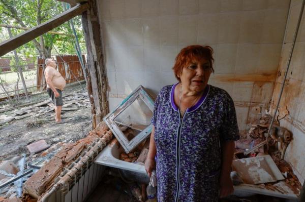 A woman inside her damaged flat. Her husband is outside, beyond the blown out window