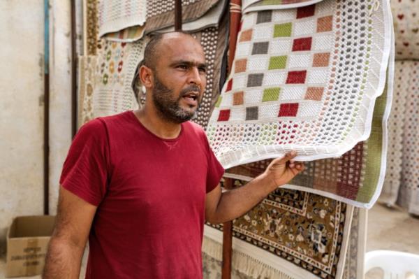 A merhcant speaks, holding a tablecloth displayed in his stall