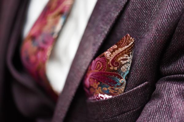 a closeup shot of a deep red jacket paired with a white shirt and a floral tie and pocket square